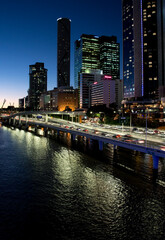 Brisbane Australia at night with the Brisbane river in the foreground and the city skyline and traffic in the background

