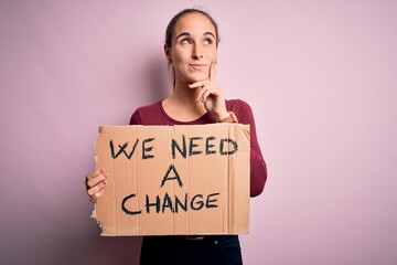 Young beautiful activist woman asking for change protesting holding banner with message serious...