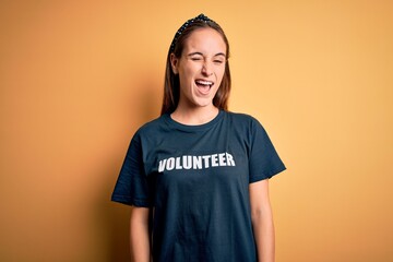 Young beautiful woman wearing volunteer t-shirt doing volunteering over yellow background winking...