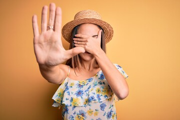Young beautiful woman wearing casual t-shirt and summer hat over isolated yellow background covering eyes with hands and doing stop gesture with sad and fear expression. Embarrassed and negative.