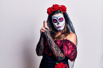 Young woman wearing day of the dead costume over white holding symbolic gun with hand gesture, playing killing shooting weapons, angry face