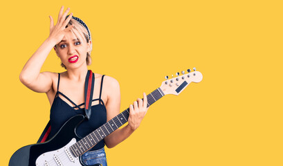 Young beautiful blonde woman playing electric guitar stressed and frustrated with hand on head,...