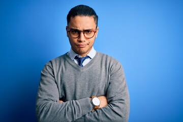 Naklejka premium Young brazilian businessman wearing tie standing over isolated blue background skeptic and nervous, disapproving expression on face with crossed arms. Negative person.