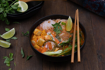 Thai vegan red curry woth tofu, noodles, beans and carrots on wooden table, copy space