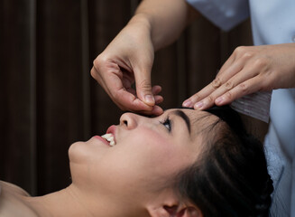 Obraz na płótnie Canvas woman lying on a table in an alternative medicine spa having an acupuncture and reiki treatment done on her face by an acupucturist