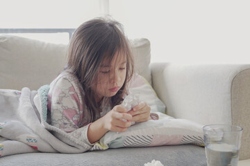 Mixed Asian sick girl having chewable pills and lying on sofa  at home, heath care concept