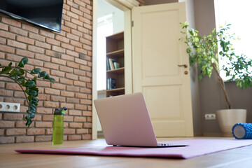 Online workout at home gym concept. Laptop computer on yoga mat on floor in living room in modern apartment interior. Internet fitness training classes remote technology video sport exercises routine