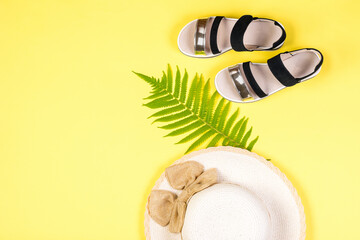Black sandals, a palm leaf and a hat on a yellow background.