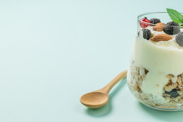 Yogurt, granola and berries in a glass and a wooden spoon.