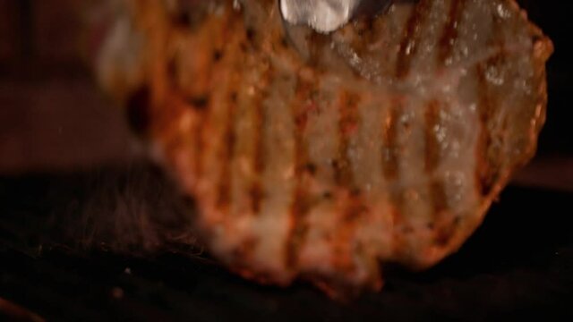 Slow-motion video. Close-up of a steak being turned over on the grill. Flames on the steak. Cooking meat on a professional grill. Kitchen, restaurant.