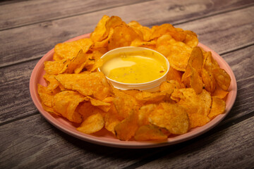 Potato chips on a round platter and a saucepan with cheese sauce. Close up.