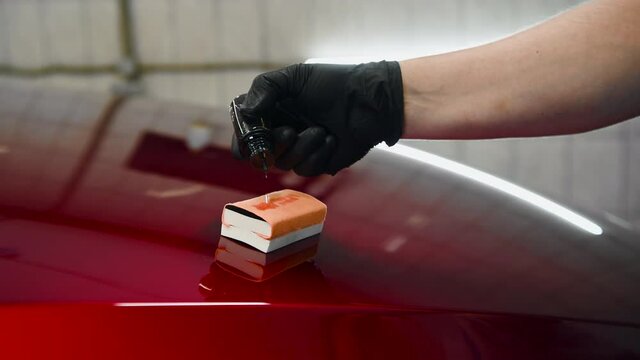 Close-up of a man hand dripping liquid coating on a sponge applicator on a car bonnet. Preparing for applying special coating on a car surface.