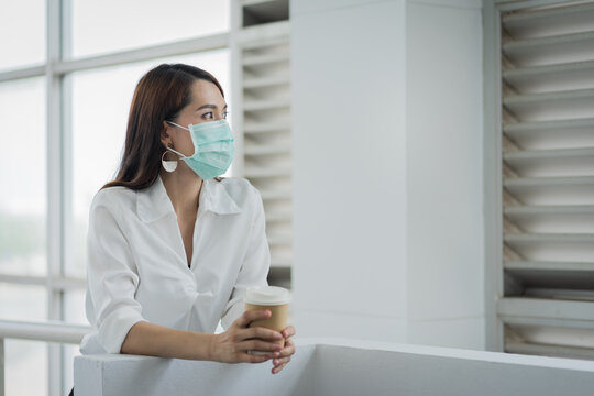 ortrait of a business woman with business suit wears face mask holds morning coffee cup in company building ready for work. A middle age woman with face mask to protect COVID-19 pandemic. stock photo