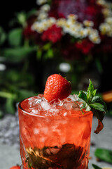 Strawberry Mojito. Cold summer mojito cocktail with strawberries, mint, lemon and ice in a glass on a table. on a dark background