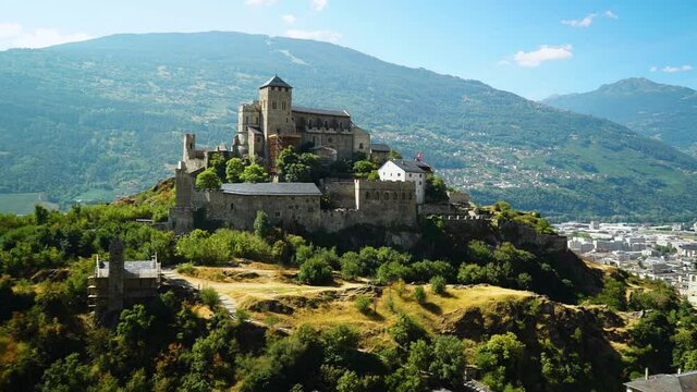 Ancient medieval castle stands atop hill in Swiss Alps with beautiful mountains and valley