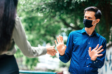 Stop it. Young man in mask refusing hand shake with his friend, woman to protect himself from...