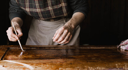male artisan paints a wooden plank of solid wood, restoration of antique furniture