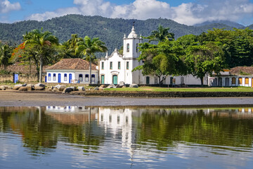 View of colonial church Igreja Nossa Senhora das Dores (Church of Our Lady of Sorrows) with water reflections and mountains in background in historic town Paraty, Brazil