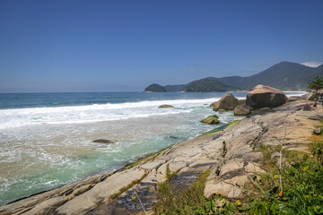Fototapeta na wymiar View along beautiful coastline with rock slabs and mountains in the background, Picinguaba, Brazil