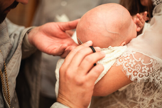 The baptism of a child. The godmother holds the child in her arms. Closeup photo, priest cuts hair
