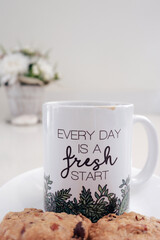 Coffee mug with inspirational message with cookies and a flower pot in the background. Every day is a fresh start. Copy space.