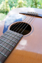 Closeup of acoustic guitar with nature background and reflection of clouds on pickguard