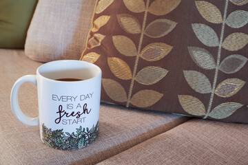 Coffee mug with inspirational message on couch with throw pillows. Every day is a fresh start. Copy space.