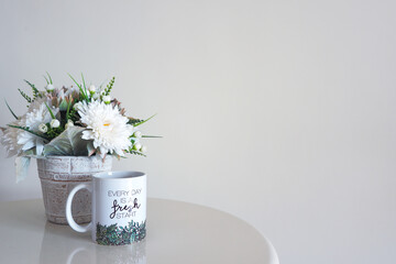 Wall mockup with coffee mug with inspirational message and pot of flowers on a table. Copy space.