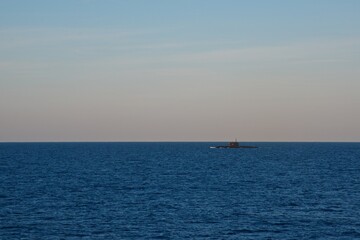Obraz premium The submarine is surfaced in the open sea in the early morning. Seascape. Clear sky over the dark blue sea.