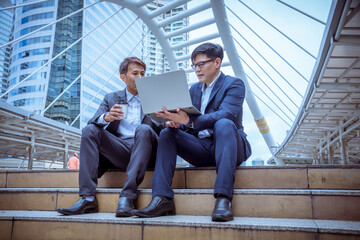 Businessmen sit on stair working with laptop discussed together about business plan with happy face.