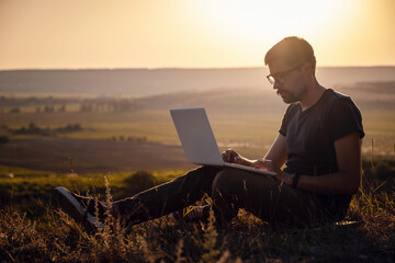 man with laptop sitting on the edge of a mountain with stunning views of the valley