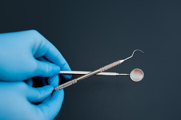 dental mirror and probe in the hands of a doctor in gloves on a smooth dark background, space for text, medical layout