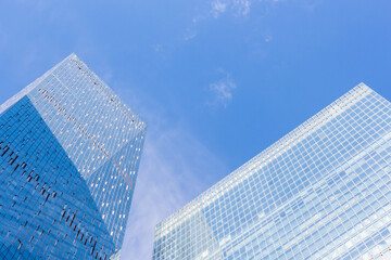 Fototapeta na wymiar Low angle view of large skyscrapers covered with glass. Blue sky with some white clouds in the background. Modern office buildings theme.