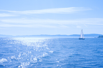 Beautiful seascape with calm blue sea with shiny water surface and sailing boat, vacation on sunny islands. Background with glowing sea and yacht