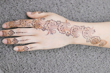 Carefully painted intricate design using henna, Mehndi art, on the hand of young Indian woman before a Vivaah-Indian Wedding. Background bokeh of wedding sari. Focus on hand.