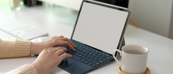 Female entrepreneur hands typing on mock-up tablet keyboard with coffee cup and computer device on table