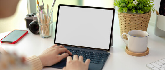 Female typing on mock up tablet with keyboard on white office desk with supplies and decorations