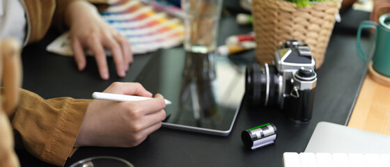 Female designer working with digital tablet on black table with camera and designer supplies