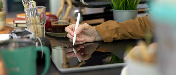 Female designer working with digital tablet on black table with painting brushes and designer supplies