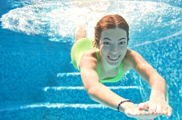 Child swims underwater in swimming pool, happy active teenager girl dives and has fun under water,...
