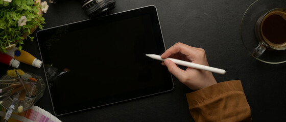 Female designer drawing on digital tablet with stylus pen on worktable with painting tools