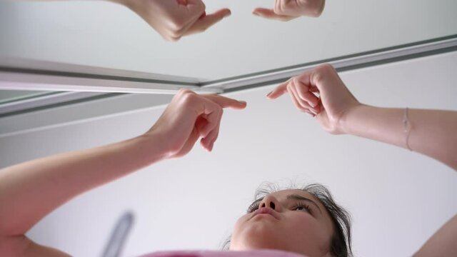 schoolgirl with ponytail pops zits on forehead with fingers in front of mirror and gets upset in bathroom close low angle shot