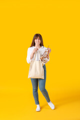 Beautiful young woman with cotton flowers and shopping bag on color background