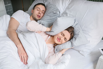 Young irritated woman in bed with snoring husband