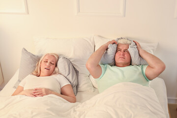 Mature irritated man in bed with snoring wife