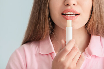 Beautiful young woman with lip balm on light background, closeup