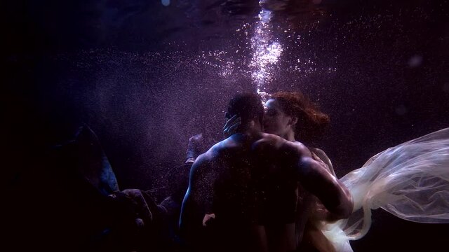 woman and man are holding breath underwater, floating and caressing each other
