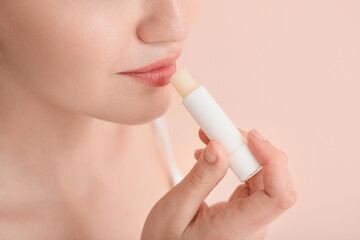 Beautiful young woman with lip balm on color background, closeup