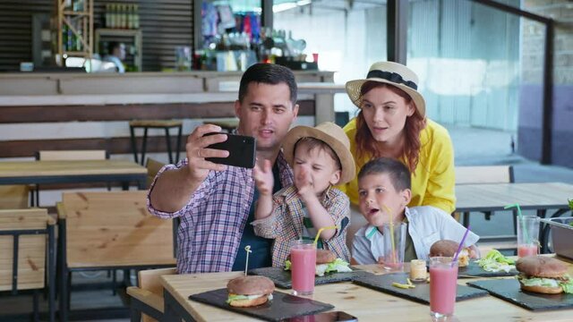 Fast Food Party, Cheerful Family Cheerful Parents Loving Mom And Dad With Male Children Enjoy Rest In Restaurant Or Cafe Eating Burgers With French Fries And Communicate With Friends Over Phone Using