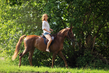 Beautiful young girl with blond hair in a jacket with a shorts, smiling and riding her horse. Equestrian, lifestyle.